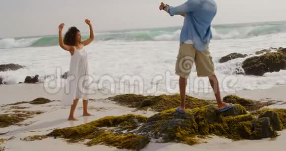 非裔美国人男子点击海滩上妇女手机照片的后视图视频的预览图
