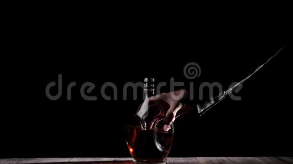 豪华白兰地穿黑色衬衫的人把一个圆形的瓶子放在木桌上背景是黑色的白兰地白兰地嗅探器视频的预览图