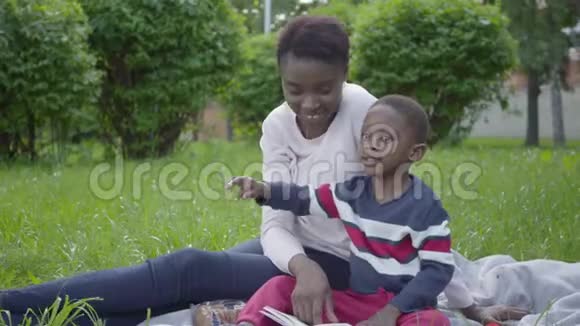 漂亮的非裔美国女人和她的小儿子坐在公园的毯子上年轻的母亲试图视频的预览图