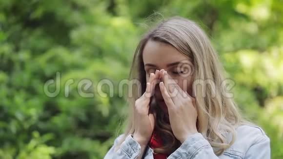 年轻女子站在公园的背景上打喷嚏和揉鼻子过敏性鼻炎人过敏的概念视频的预览图