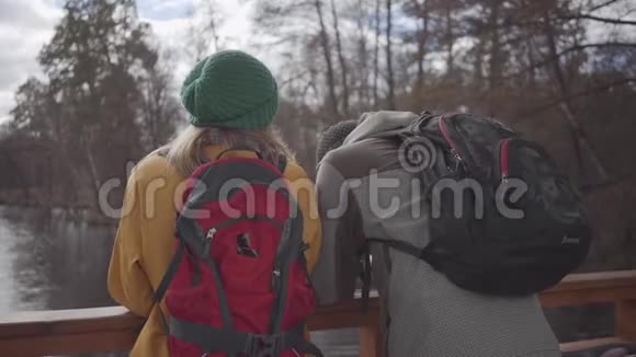 两个穿着夹克和帽子的游客站在河边的桥上谈论和享受自然a的假期视频的预览图