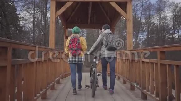 两个年轻的游客走在公园的桥上背着背包男人牵着自行车女人视频的预览图