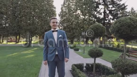 英俊的新郎穿过公园衣冠楚楚的男人结婚纪念日慢动作视频的预览图