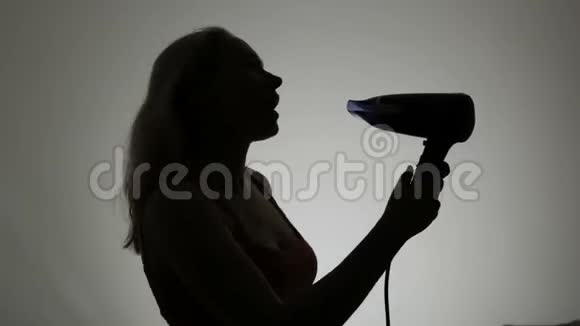 一位留着长发的年轻女子的剪影擦干头发在吹风机里唱歌就像在麦克风里一样视频的预览图