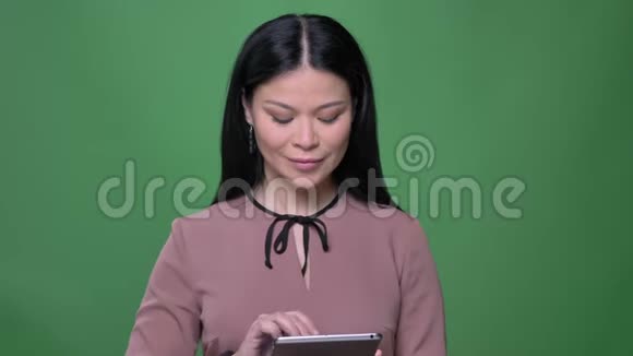 用平板电脑为年轻有魅力的黑发亚洲女性拍摄特写镜头并在镜头中显示蓝色的彩色屏幕视频的预览图
