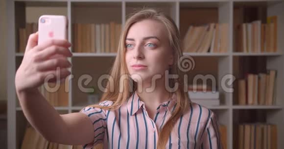 高校图书馆年轻漂亮的高加索女学生在电话里自拍的特写照片视频的预览图