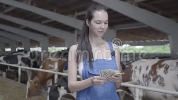 奶牛场上年轻漂亮的女职工微笑着数钱的画像积极的农民从农场得到收入视频的预览图