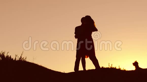 恋爱中的情侣在日落和接吻时跳舞剪影爱的男人和女人与狗跳舞剪影缓慢视频的预览图