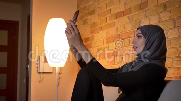 戴头巾的穆斯林成年女性的特写镜头坐在沙发上用电话视频通话视频的预览图