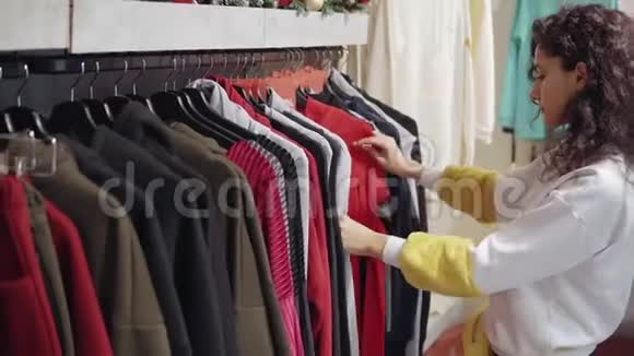 女人在商店里看着打折的衣服带着裤子和毛衣移动衣架视频的预览图