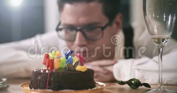 年轻迷人的男人独自坐在桌子旁伤心地吃着烧过的蜡烛上的巧克力背景耀斑故障视频的预览图