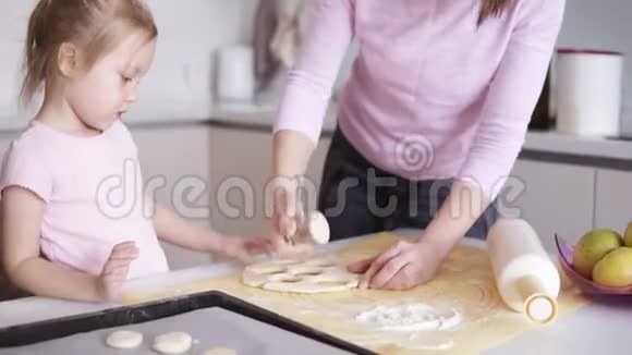 一位母亲和她金发的女儿在厨房准备饼干小女孩用金属形状切割饼干视频的预览图