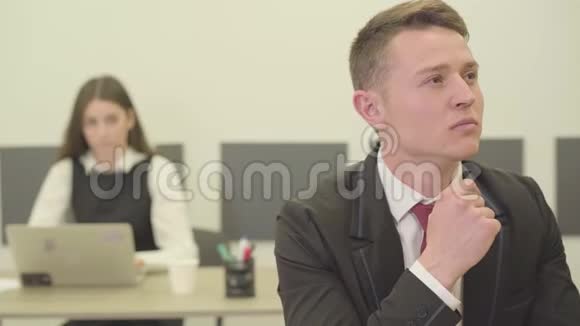 肖像英俊体贴的年轻人坐在办公室的前台而他的女同事则穿着正式服装视频的预览图