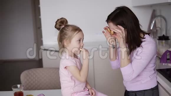 年轻的母亲正在厨房里和她的小女儿开玩笑从面包圈里拿出眼镜微笑着做视频的预览图