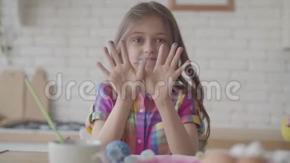 肖像有趣可爱情绪化的小女孩双手拿着蓝色的油漆在厨房里做了一个镜头的鬼脸视频的预览图