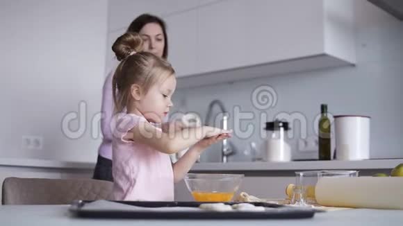 金发的小女孩在厨房帮她妈妈为饼干准备面团妈妈干净的女儿手视频的预览图