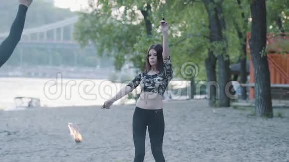 戴着面具的年轻可爱女人在树前用火焰表演节目的肖像熟练的火技艺术家展示视频的预览图