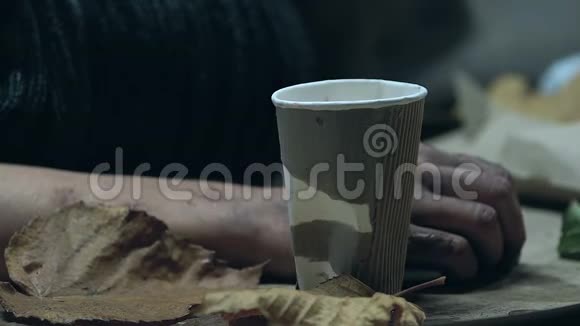 无家可归的人在寒冷的街道上颤抖乞求金钱硬币掉进纸杯里视频的预览图