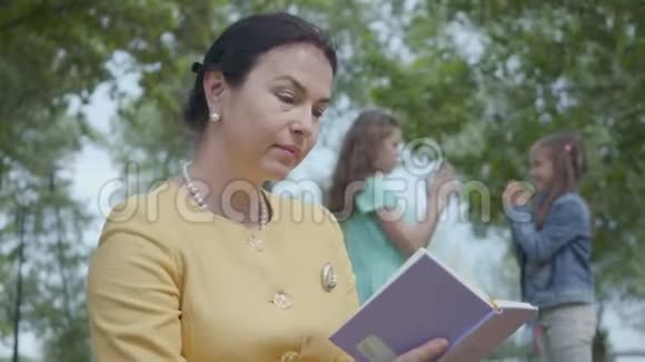 一位优雅的高级妇女在前景公园里读这本书的肖像两个模糊的数字视频的预览图
