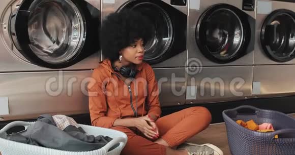 年轻的黑人非洲裔美国妇女等待她的衣服在自动洗衣店洗视频的预览图