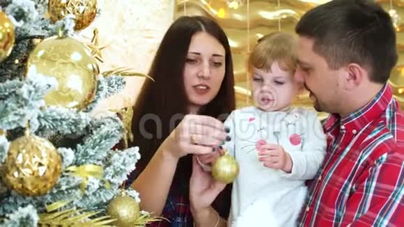 年幼的父母带着蹒跚学步的女儿在家的圣诞树上装饰视频的预览图