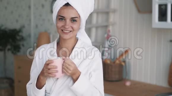 穿着浴袍的女孩的肖像头上戴着毛巾微笑喝着咖啡慢动作视频的预览图
