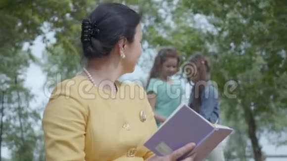 一位优雅成熟的女人在公园的前景中阅读这本书的肖像两个模糊的数字视频的预览图