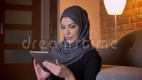 在平板电脑上戴着头巾上网的穆斯林成年女性的特写肖像坐在地板上视频的预览图