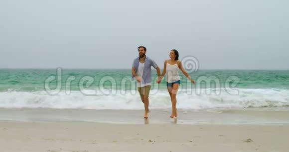 高加索夫妇手牵手在海滩上奔跑的正面景色视频的预览图