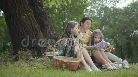 肖像可爱的高级女人坐在公园树下的毯子上看书两个可爱的视频的预览图