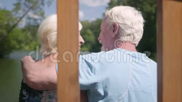 一对幸福成熟的夫妇坐在河边的长凳上欣赏大自然年长的女人吻她视频的预览图