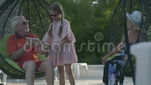 成熟的夫妇坐在挂椅上一起在酒店综合体放松可爱的小女孩站在附近视频的预览图