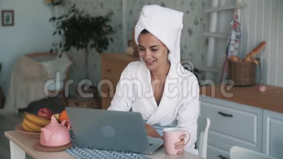 头戴毛巾的女孩在笔记本电脑上视频聊天喝茶慢动作视频的预览图