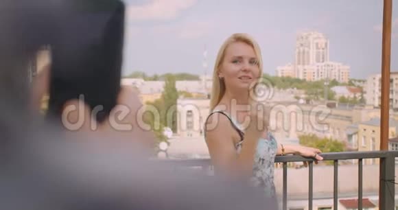 一幅白种人成年女性的特写照片她站在房子的阳台上被一个男孩用电话拍下视频的预览图