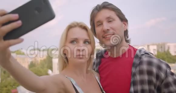 一对幸福迷人的白种人夫妇在电话拥抱中自拍站在房子的阳台上视频的预览图