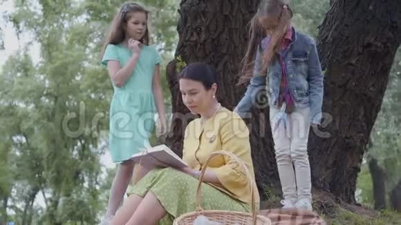 优雅的高级女人坐在公园树下的毯子上看书两个可爱的孙女视频的预览图