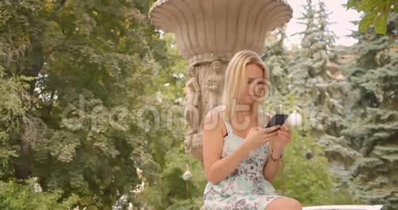 一幅白种人成年女性在户外用电话坐在公园里等待男友的特写照片视频的预览图
