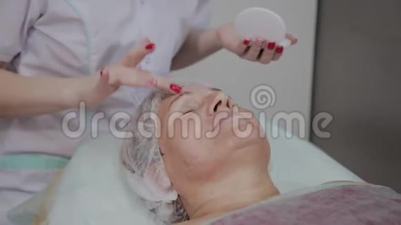 专业美容师对美容院的老年妇女使用保护霜视频的预览图