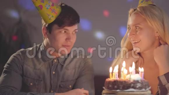 戴着生日帽的金发女孩吹灭蛋糕上的蜡烛年轻人坐在附近女人过生日视频的预览图