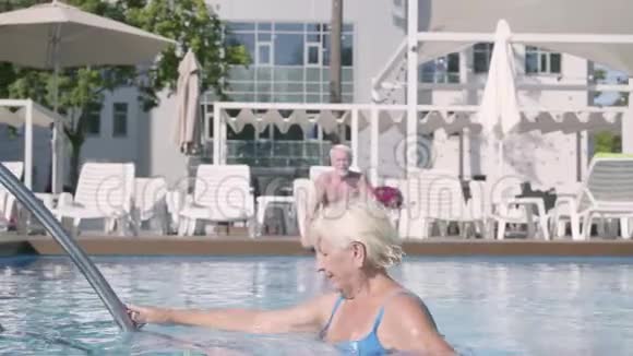 快乐的成熟夫妇一起在酒店综合体的游泳池放松漂亮的高级女性日光浴和挥手视频的预览图