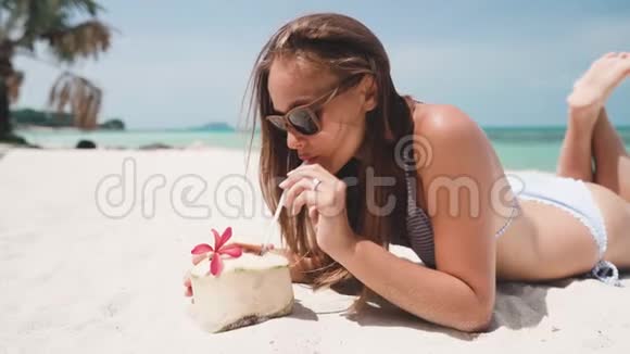 女人躺在沙滩上喝着椰子直视镜头视频的预览图