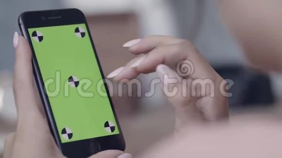 年轻女性的双手完美的美甲手握智能手机并在彩色键绿色屏幕上滑动视频的预览图