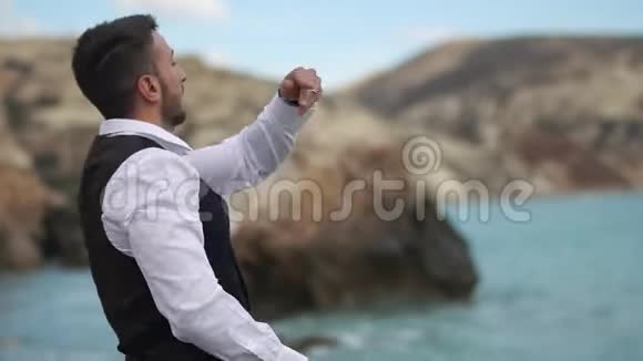 长着胡子的英俊小伙子在海边和山上向水里扔石头慢动作塞浦路斯帕福斯视频的预览图