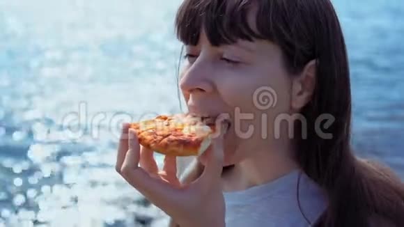女孩咬掉一块比萨饼然后在大海的背景下咀嚼它视频的预览图