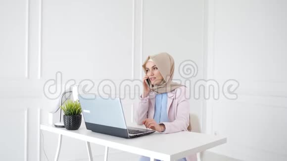 迷人的放松的穆斯林妇女正在谈论手机坐在她的工作场所视频的预览图