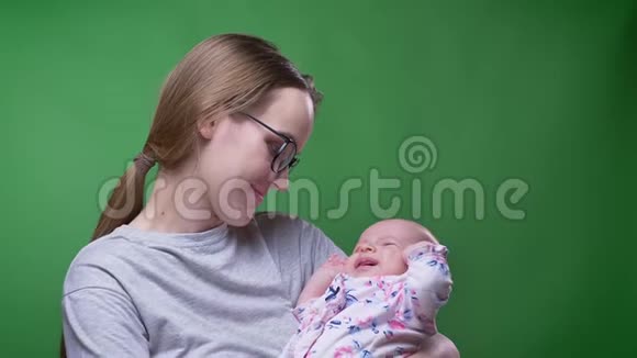 在绿色背景下美丽的母亲抱着她可爱美丽的新生女儿亲吻她的特写肖像视频的预览图