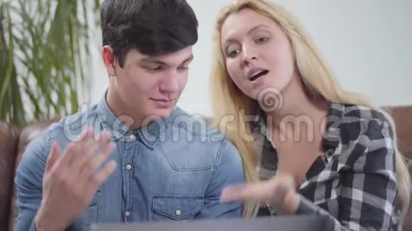 一对年轻夫妇坐在家里的笔记本电脑前一个黑发男人和一个金发女人的肖像在讨论这个项目视频的预览图