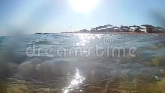 一台摄像机拍摄的视频它在海岸附近的海浪上拍打着上面有一把茅草伞和一把躺椅一个超宽的圆形视频的预览图