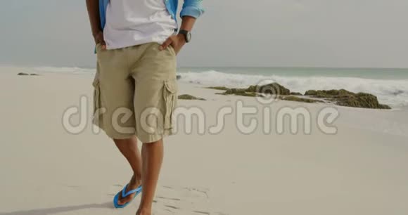 美国黑人男子在海滩上双手插袋行走的正面景色视频的预览图