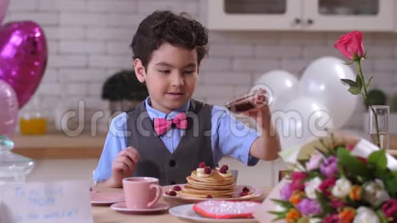 快乐的小男孩在煎饼上倒枫糖浆视频的预览图